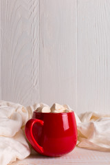 Red mug with cocoa and marshmallows on a white table scarf background. Autumn mood, a warming drink. Copy space.