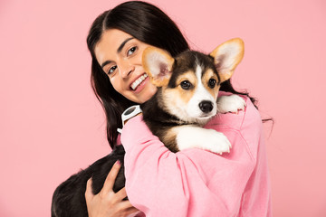 cheerful girl holding Welsh Corgi puppy, isolated on pink