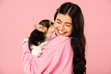 cheerful woman holding Welsh Corgi puppy, isolated on pink