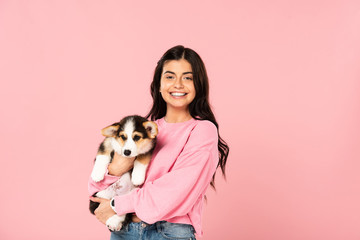smiling woman holding Welsh Corgi puppy, isolated on pink