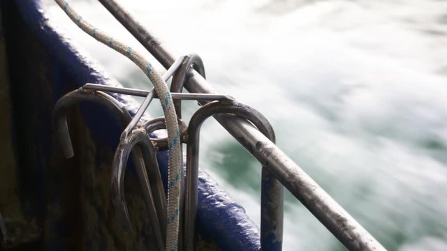 A daylight extreme closeup shot of a stainless steel anchor with four hooks and tied to a rope clinging at the metal bars at the side of the boat..