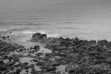 Fisherman is sitting on the rocks. Very dramatic black and white scene.