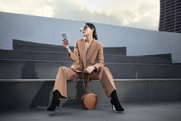 Portrait of a successful business woman sitting on stairs. the phone is in her hands. City background