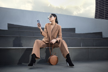 Portrait of a successful business woman sitting on stairs. the phone is in her hands. City...