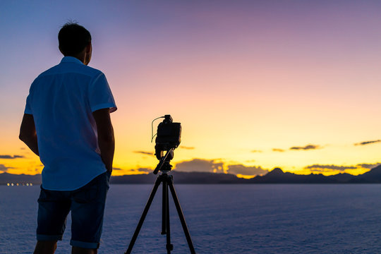 Bonneville Salt Flats near Salt Lake City, Utah at colorful twilight with purple sky and man standing by tripod with camera doing time lapse photography