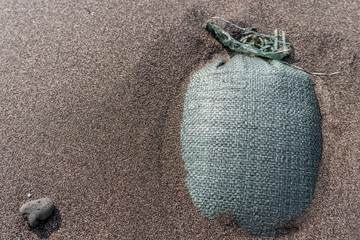 Hidden bag on the beach. Black sand around strange bag. Very suspicious object.