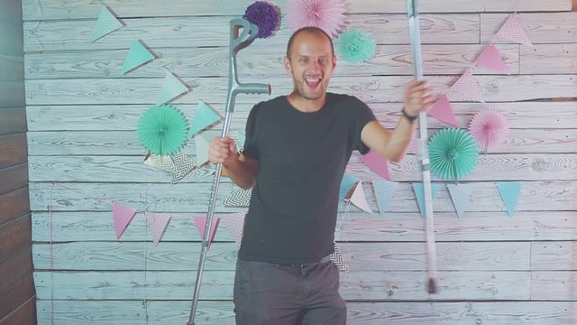 happy man dancing with crutches in his hands in a festive interior