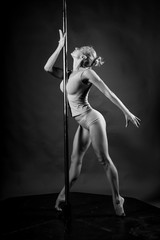 Beautiful athletic busty elegant blonde girl performs artistic elements of an exotic dance on a gray background. Health, lifestyle, sports black and white monochrome design. Copy space.