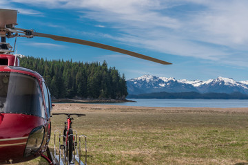 Red helicopter and bicycle is waiting for passengers. On a background is green forest, snowy...