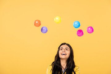happy attractive girl with colorful balls, isolated on yellow