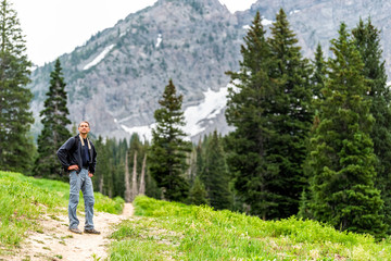 Albion Basin, Utah pine trees and man standing on summer dirt road trail in 2019 in Wasatch mountains with rocky snowy Devil's Castle mountain