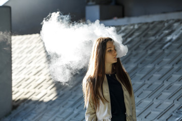 Vape teenager. Young cute girl in  casual clothes smokes an electronic cigarette outdoors in summer...