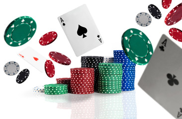 Multicolored chips in piles are standing on a surface, some of them are flying apart with playing cards, aces. Isolated on white background.