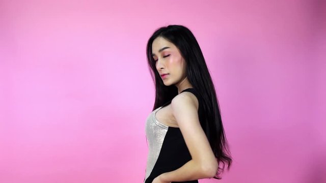 Transgender young Asian woman model turns and flips throw her long black hair as she poses in the studio pink background