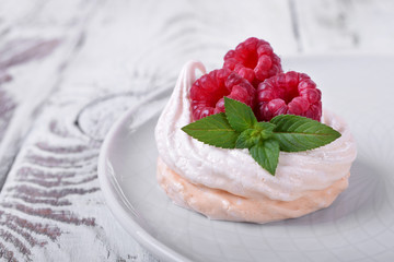 Mini Pavlova cake topped with raspberries and mint on white wooden table