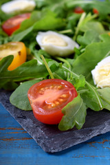 Salad with arugula, cherry tomatoes and quail eggs served on a slate plate