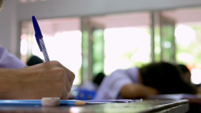 Asian high school students in a white school uniform are doing examinations. They are serious and tired.