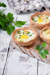 Baked rye tartlets with cheese and quail eggs on white wooden table