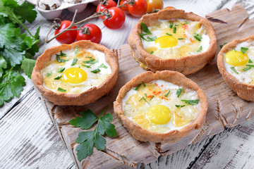 Baked rye tartlets with cheese and quail eggs on white wooden table