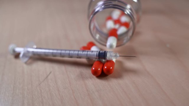 Close up of a hypodermic needle and red pills. Medical image suitable for health or addiction concept.