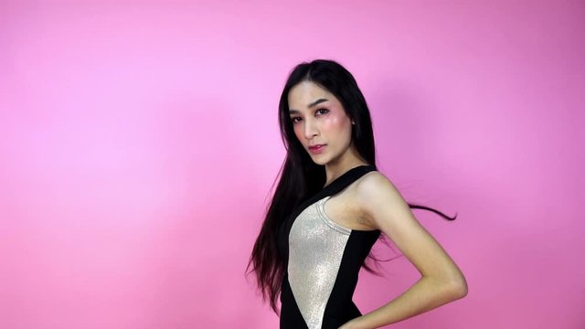 Beautiful female model flips her long straight black hair fashion make up face to look at the camera in a photo shoot over pink backgrounds