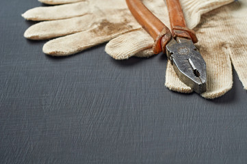 Pair of dirty textile protective gloves for repair or other hard works near old messy pliers with...