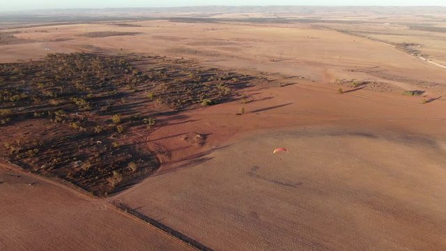 Aerial cinematic drone shot of paramotor extreme sport  flying over wide nice field in South Australia