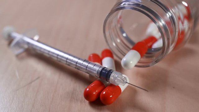 Close up of a hypodermic needle and red pills. Medical image suitable for health or addiction concept. Rack focus technique