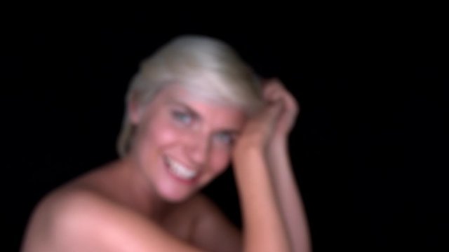 young blond model girl looks into the camera and smiles. Picture blurred then sharp. Slow motion with black background.