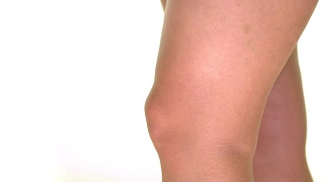 Caucasian woman has knee pain and massages her knee herself. Close Up view with white background. Slow motion.