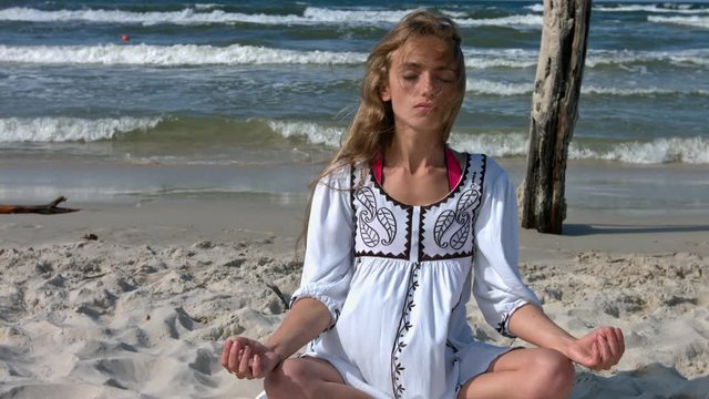 Young woman is meditate at the beach. Enjoing the sunlight and the noise of waves in the background. Closeup. Slow Motion.