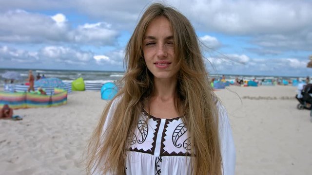 Beautiful girl on the beach, smiling towards the camera while waving her long hair.