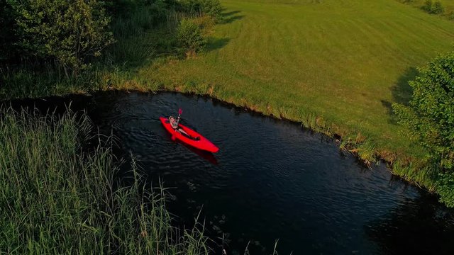 An aerial view of a young ,beautiful and sexy woman wearing bikini ,Canoeing/kayaking in a red boat in the silent lake amidst beautiful fields during sunset.