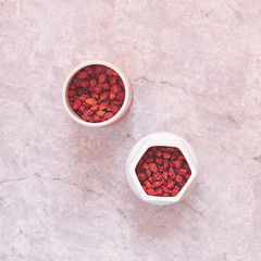Dried rosehip berries are in various containers on a cement background.