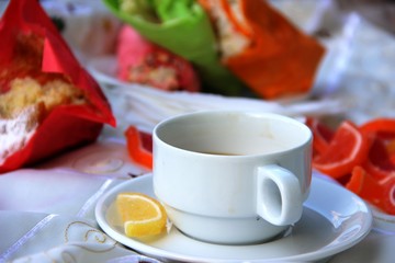 Cup of coffee, a bright yellow slice of marmalade on a saucer, a cupcake and sandwiches blurry. picnic in nature