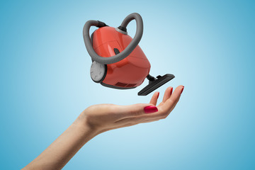 Female hand with red vacuum cleaner on blue background