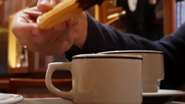 Close shot of female hand dipping a traditional sweet fried churros in hot cocoa chocolate sauce, Spanish and Mexican delicacy for dessert