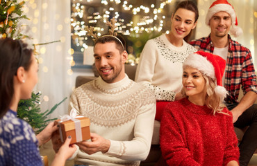 celebration and holidays concept - happy friends with glasses celebrating christmas at home party and giving presents