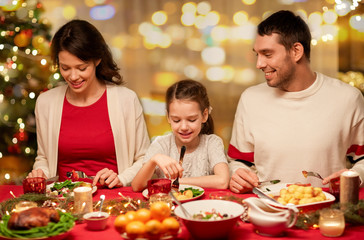 holidays, family and celebration concept - happy mother, father and little daughter having christmas dinner at home