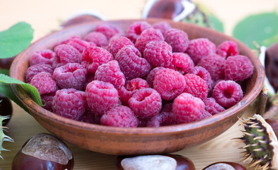 Fresh raspberries background closeup photo. Red raspberries in ceramic bowl on wooden table, chestnuts. 