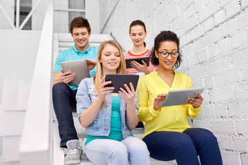 education, technology and learning concept - group of happy international high school students or classmates with tablet pc computers sitting on stairs