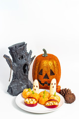 Halloween healthy organic treat with bananas, mandarines and apples on a white plate with ornaments around with empty space on the top for text and graphics.