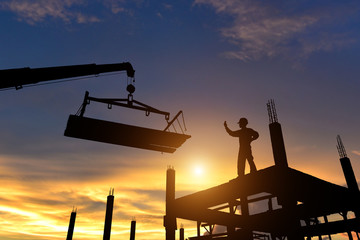 Workers in safety equipment installed concrete panels in the construction site at sunset.