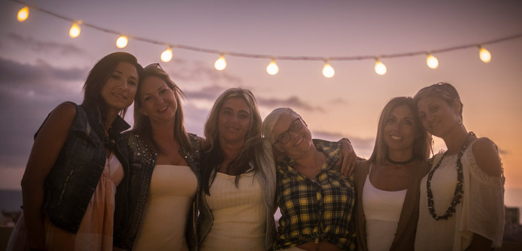 Group of different ages generations friends female people hug and enjoy with love the friendship together in the evening outdoor - sunset sky in background