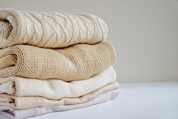 Warm sweaters in a pile, knitted texture, minimalism lifestyle, capsule wardrobe, autumn-winter season. With selective focus and copy space.