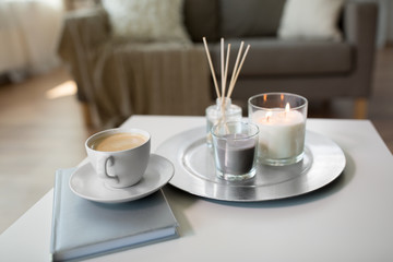 hygge and aromatherapy concept - coffee, candles, book and aroma reed diffuser on table at home