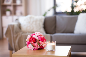 decoration, hygge and cosiness concept - burning fragrance candle and flower bunch at cozy home