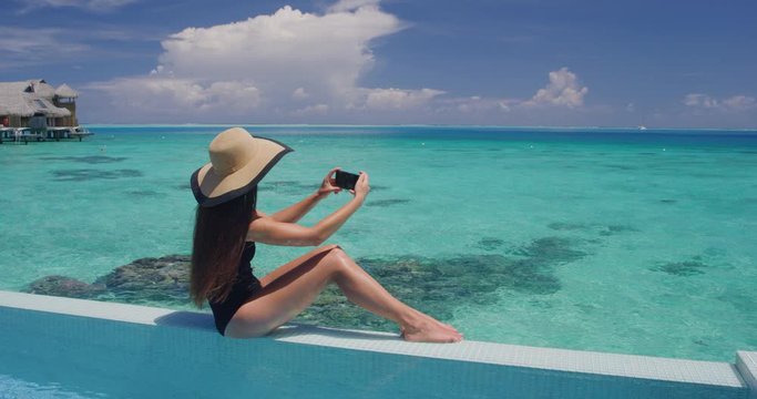 Beach Vacation Woman taking photo pictures using mobile cell phone app on holidays by pool by tropical ocean coral lagoon on travel holidays. Slow motion video shot on RED Cinema Camera.