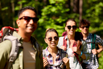 travel, tourism, hike and people concept - group of friends walking with backpacks in forest