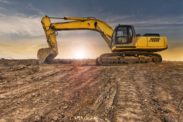 Excavator at late afternoon on dry muddy ground - obrazy, fototapety, plakaty